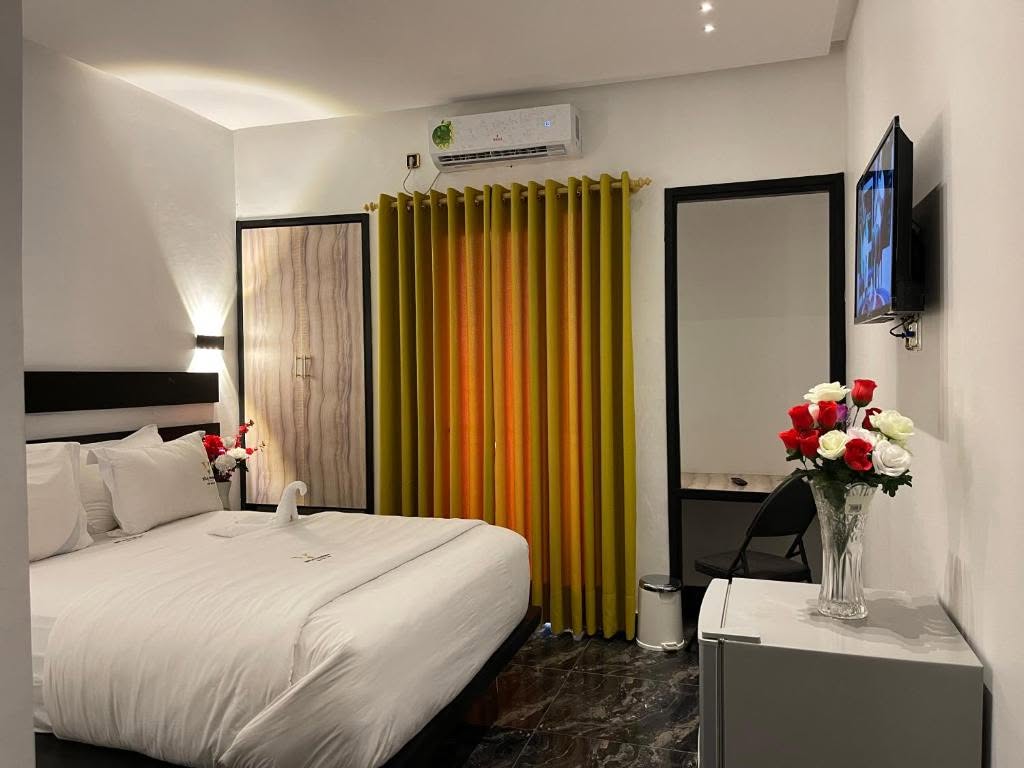 Chambre Confort avec grand lit, rideaux dorés et télévision murale